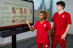 Two nursing students examine a slide titled "Review of Anatomy and Physiology."